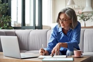 content woman at coffee table with laptop taking notes